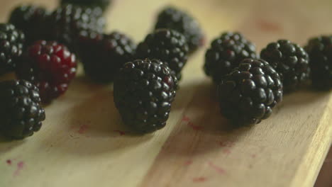 Slow-motion-footage-of-a-bunch-of-plump,-ripe-blackberries-dropping-on-to-a-wood-cutting-board