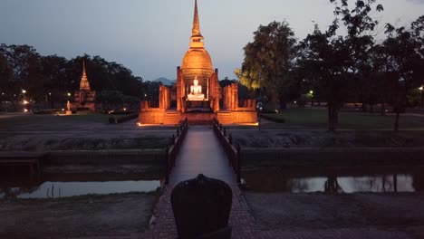 Estatua-Del-Parque-Histórico-De-Sukhothai-Iluminada-Bajo-Un-Cielo-Estrellado-Resplandor-Misterioso-Con-Una-Silla-De-Piedra-Para-Sentarse-Frente-Al-Templo-Del-Señor-Buddha