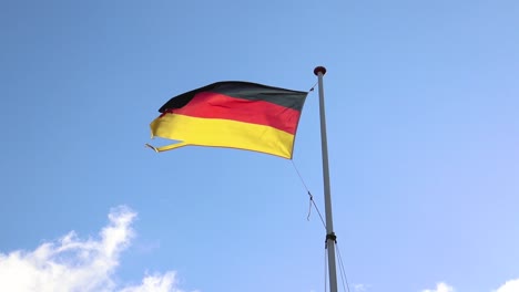 Wind-Weht-Die-Deutsche-Flagge-Mit-Sich-Bewegenden-Wolken-Und-Blauem-Himmel-Im-Hintergrund