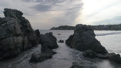 Aerial-cinematic-shot-rocks-formations-and-the-sea-in-Zicatela-beach,-Puerto-Escondido,-Oaxaca
