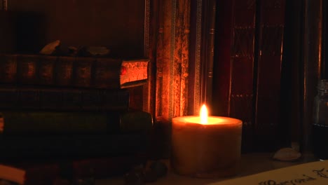 Close-up-background-of-an-ancient-library,-next-to-a-frieplace,-with-old-books,-old-paper,-ink,-stones,-and-a-candle-with-flickering-flame