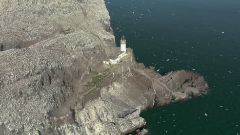 Eine-Luftaufnahme,-Die-Bass-Rock-Und-Leuchtturm-Umkreist,-Während-Basstölpel-Seevögel-An-Einem-Sonnigen-Tag-Ihre-Inselkolonie-Umkreisen,-East-Lothian,-Schottland