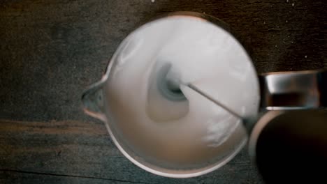 Draufsicht-Auf-Kaffeesahne-Mit-Elektrischem-Milchaufschäumer,-Der-Hineingeht-Und-Milch-Auf-Dunklem-Hintergrund-Mischt