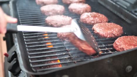 Lid-opening-on-grill-and-spatula-flipping-alternative-meat-burger-patties-on-a-barbecue,-wide-shot-panning-with-flame-in-slow-motion-4k