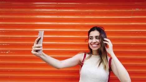 Zeitlupe:-Schönes-Junges-Mädchen-Macht-Selfie-Mit-Smartphone-Vor-Orangefarbenem,-Rotem-Hintergrund