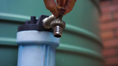Dripping-spigot-on-outdoor-water-tank-turned-off-by-male-hand,-close-up