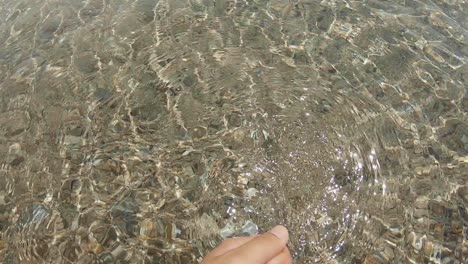 Males-hand-grabbing-clear-water-with-sand-on-the-ground