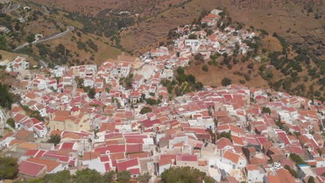Backwards-aerial-flying-high-above-Ioulida-town-in-Kea-with-landscape-CROP
