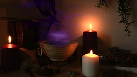 Detail-of-a-potion-making-witch-room,-with-purple-steam-coming-out-from-a-wooden-bowl,-animal-teeth-hanging-from-it,-candles-with-flickering-flames,-old-books,-glasses-and-herbs-in-the-background