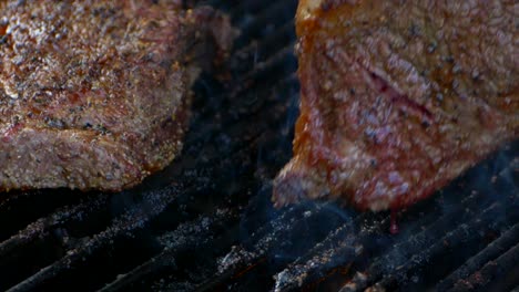 A-fork-turns-a-nearly-cooked-juicy-rib-eye-steak-on-a-grill-as-blood-drips-from-it-and-flames-shoot-up-in-slow-motion