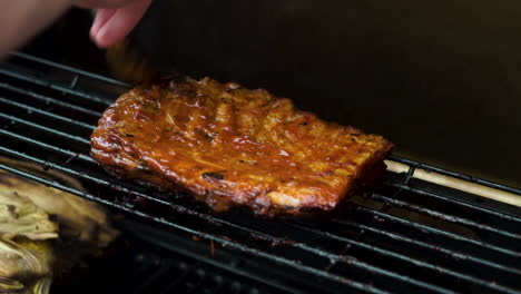 medium-shot-of-a-slow-cooked-pork-belly-being-cooked-on-a-barbecue,-BBQ,-having-miso-barbecue-sauce-brushed-on-with-a-male-hand