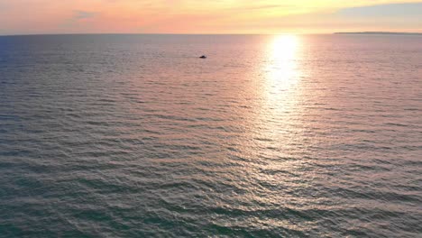Drone-flies-over-boat-in-the-ocean-on-colorful-sunset