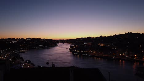 Golden-sunset-lights-western-sky-aglow-over-mouth-of-Douro-River-in-Porto,-Portugal-as-lights-illuminate-city-in-silhouette