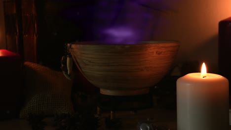 Detail-of-a-potion-making-witch-room,-with-purple-steam-coming-out-from-a-wooden-bowl,-animal-teeth-hanging-from-it,-candles-with-flickering-flames,-old-books-in-the-background,-dust-flying-around