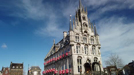 Gouda-city-in-The-Netherlands,-Het-Oude-Stadhuys-at-the-market-place-with-blue-sky-and-some-people