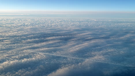 Vista-Increíble-Desde-La-Cabina-De-Un-Avión-Que-Vuela-Alto-Por-Encima-De-Las-Nubes-Dejando-Un-Largo-Rastro-De-Aire-De-Vapor-De-Condensación-Blanco-En-El-Cielo-Azul