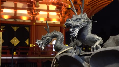 Pequeños-Dragones-De-Hierro-Frente-Al-Templo-Iluminado-Del-Santuario-Sintoísta-De-Asakusa-Senso-ji-En-La-Noche,-Una-Famosa-Atracción-Turística-En-Japón,-Tokio