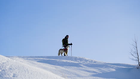 Woman-with-her-faithful-dog-on-a-top-of-a-mountain-during-winter-hiking-trip