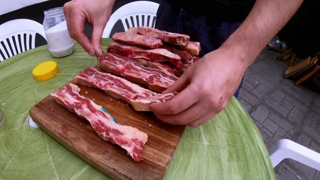 Video-of-a-white-man-putting-salt-on-the-raw-meat-on-a-wooden-board,-before-grilling