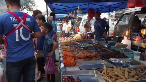 A-food-stalls-full-of-food-display-on-the-table-with-people-gathering-and-buying-while-vendor-is-standing-by