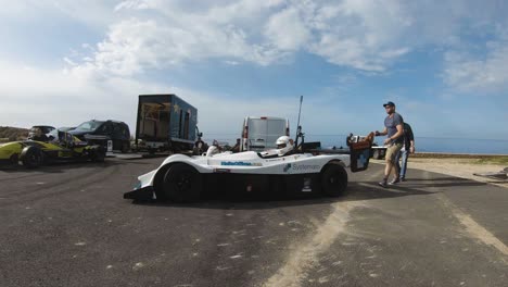 Man-Pushing-A-White-Racing-Car-To-Start-The-Engine-At-The-Hill-In-Imtahleb-Malta-On-A-Sunny-Day---GoPro-Pan-Shot