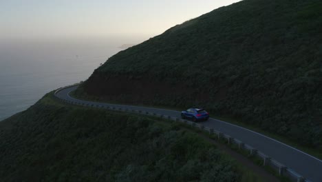 Blue-Porsche-Macan-driving-through-the-Marin-Headlands-in-San-Fransisco,-California,-at-sunset