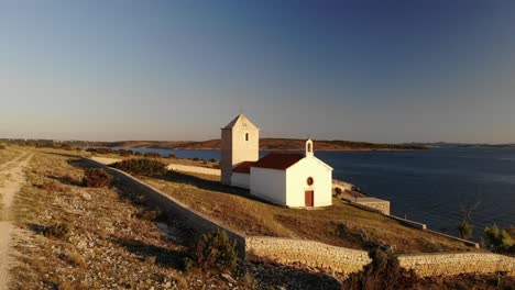 Rural-Church-on-a-tiny-island-in-sunset-near-Zadar,-Croatia,-drone-lift-off