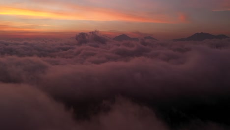 The-beautiful-fiery-orange-sunset-beyond-the-clouds-and-mountain-peaks-of-Bali,-Indonesia---Aerial-shot