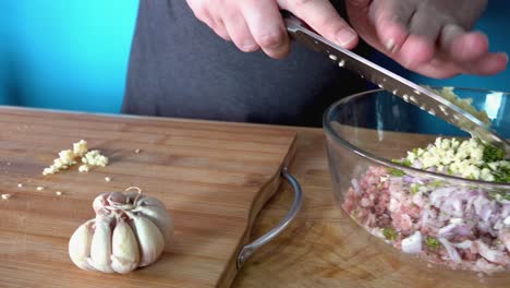 Adding-Fresh-Minced-Garlic-to-Meatball-Mixture-on-a-Wooden-Chopping-Board