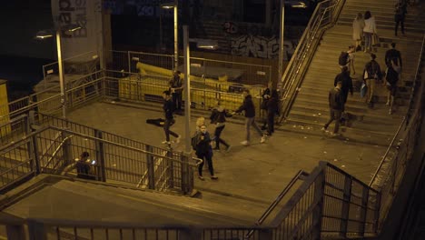 Musician-with-guitar-in-crowded-place-full-of-pedestrians-and-stairs-at-night