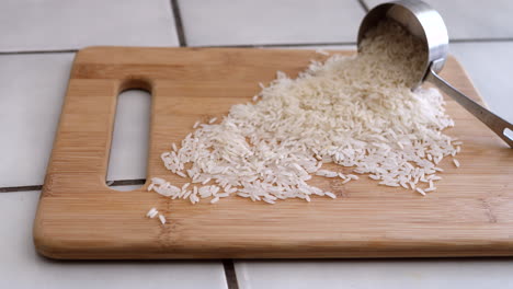 Ein-Haufen-Weißer-Reiskörner,-Der-Aus-Einem-Messbecher-In-Einer-Küche-Für-Ein-Pflanzliches-Rezept-Strömt,-Rutscht-Nach-Rechts