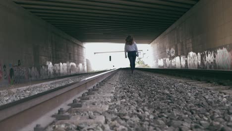 Young-woman-walks-between-the-train-tracks-in-a-tunnel-full-of-graffiti