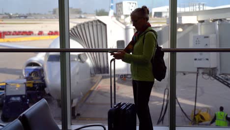 Silhouette-of-woman-traveler-with-luggage-checking-her-cellphone-in-front-of-airplane-getting-ready-to-board