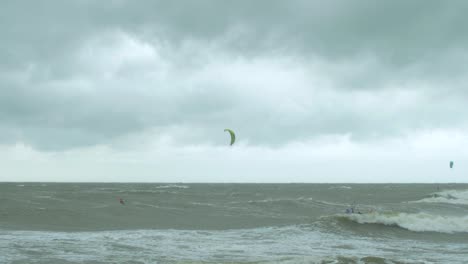 Kite-surfing-surfers-sailing-on-the-big-Baltic-sea-waves-at-Liepaja-Karosta-beach,-overcast-autumn-day,-wide-shot