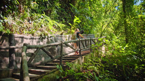 Slow-Motion-of-Young-Blonde-Tourist-Girl-Going-Upstairs-in-the-Rain-Forest-of-Arenal,-Costa-Rica
