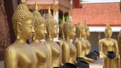 Row-of-smiling-golden-Buddha-statues-with-alms-bowl,-rack-focus