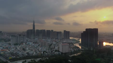 Epische-Sonnenaufgangs-Drohnenaufnahme-Von-Ho-Chi-Minh-Stadt,-Die-Auf-Wahrzeichen-Und-Central-Park-Entwicklungen-Zufliegt-Und-Mit-Der-Golden-River-Entwicklung-Mit-Sonne-Und-Reflexionen-Endet