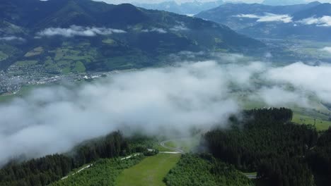 Fliegen-über-Einer-Skipiste-Im-Sommer-In-Den-Alpen-Mit-Tief-Hängenden-Wolken-über-Dem-Dorf-Darunter