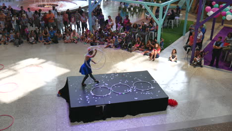 Woman-dancing,-playing-hoop,-hula-hoop-show,-outdoor-event,-gymnastics,-training-view-in-arena,-people-and-kids-watching,-audience-clapping,-applauding,-smooth-zoom-in