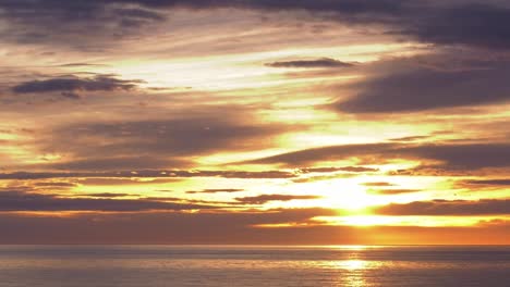 Golden-sunrise-over-ocean-timelapse-with-clouds-moving-in-dawn-skies,-wide-shot