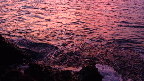 Ripply-ocean-waves-reflecting-beautiful-sunset-colors-and-hitting-on-rocks,-medium-shot