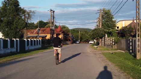 Moreni,-Romania---13-July-2020-:-Guy-wearing-black-riding-bike-on-a-country-road-at-sunset,-slow-motion