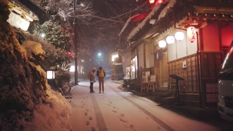 A-Couple-Standing-On-The-Street-During-The-Heavy-Snow-At-The-Kifune-Jinja-Shrine-At-Night-In-Kyoto,-Japan