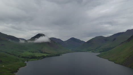 Aerial-shot-of-a-lake-surrounded-by-mountains-with-low-clouds,-grey-summers-day