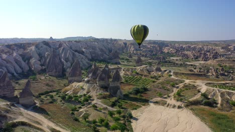 Hot-air-balloon-floating-above-Cappadocia-landscape,-pull-back-aerial
