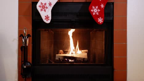 Wide-shot-of-logs-burning-in-a-fireplace-with-red-and-white-snowflake-Christmas-stockings-hanging-above
