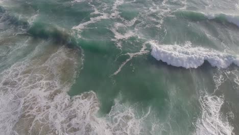 Beautiful-ocean-waves-near-shore-churn-up-the-sandy-bottom,-aerial