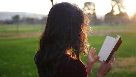 A-young-woman-reading-a-story-book-outdoors-in-the-park-at-sunset-with-light-shining-bright
