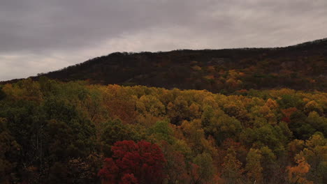 aerial-drone-shot-over-the-autumn-colored-tree-tops,-as-the-camera-pedestal-downward---tilts-up-to-reveal-the-gray,-cloudy-skies---mountains-in-Beacon,-NY