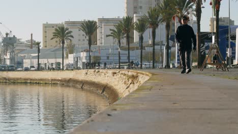 People-walking-by-the-river-on-a-sunny-morning,-promenade-view,-Portimão---Algarve